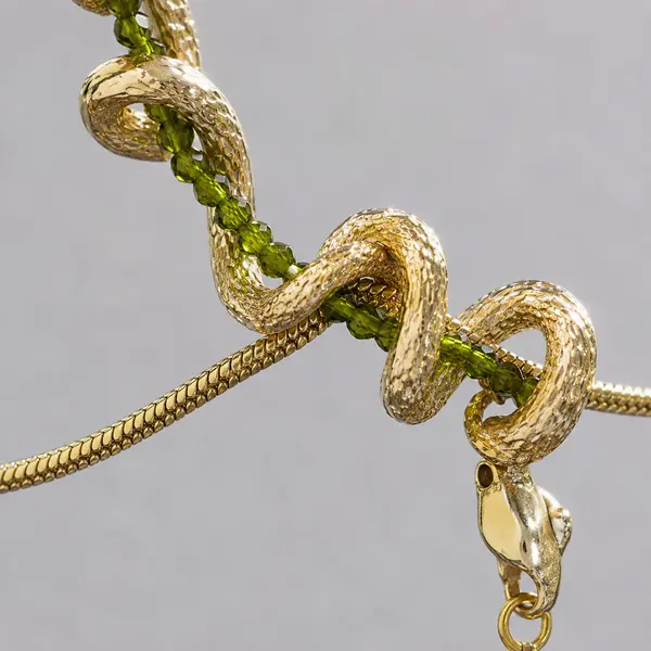 Macro detail of sculptural gold-tone serpent coils around an olive-green bead strand